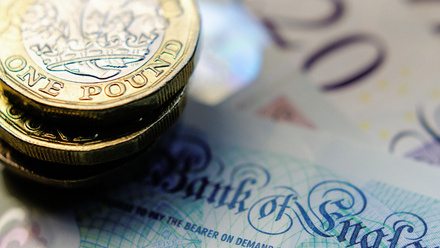 Close up on a stack of one pound coins on top of some five, ten and twenty pound notes.