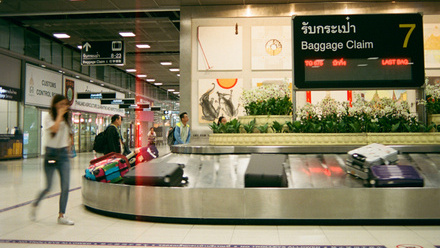 Airport baggage reclaim belt with suitcases and people standing around.