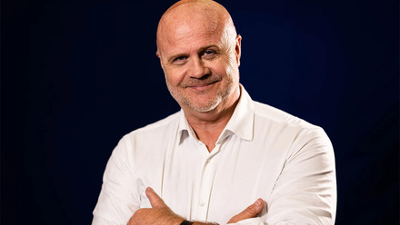 Headshot: Emyr Afan, a man with a short goatee beard and bald head, wearing a white shirt.