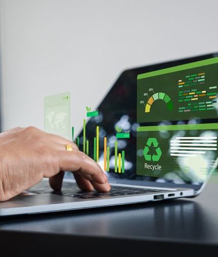 Hands on a laptop with green, sustainability-related data and text coming out of a black screen.