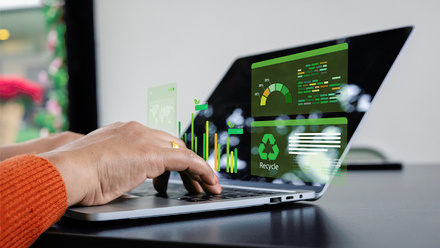 Hands on a laptop with green, sustainability-related data and text coming out of a black screen.