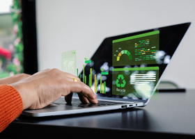 Hands on a laptop with green, sustainability-related data and text coming out of a black screen.