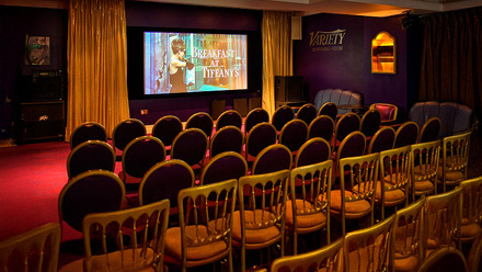 Screening room at the Soho Sanctum Hotel playing Breakfast At Tiffany's on the screen with gold curtains and rows of red chairs in the audience.