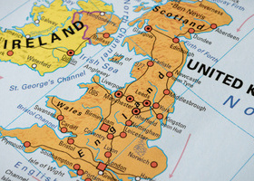 A close up of the UK and Ireland maps on a globe, with the land masses coloured in orange and yellow and key roads shown in red.