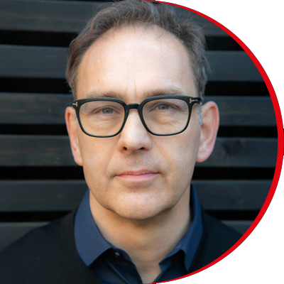 Headshot: Nigel Warner, a man with short brown hair wearing dark-framed glasses and a navy shirt.