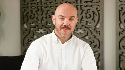 Headshot: Doug Wood, a bald man with a moustache and beard wearing a white shirt.