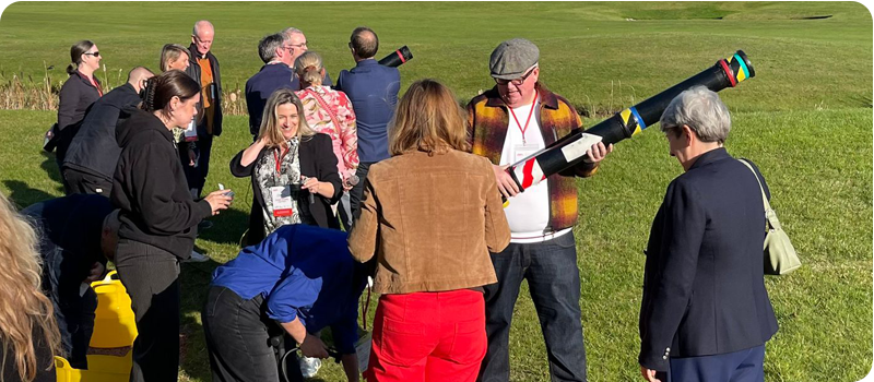 Delegates at Content Without Borders outside in a field, working together in teams to launch a toy rocket, looking engaged and amused.