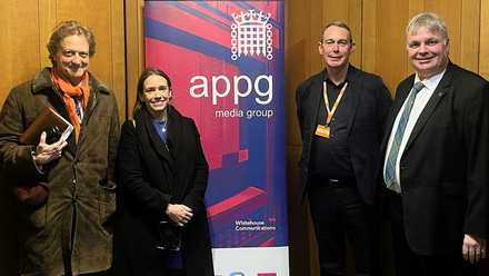 Four people stood in a wood-panelled room beside a pop-up banner with the words 'APPG Media Group' on it.