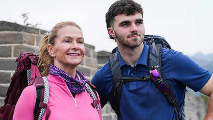 Two BBC Race Across the World contestants wearing backpacks stood in front of a mountainous background. 