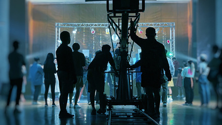 A studio space lit in blue with a large camera and dolly track in the centre and various cast and crew members.