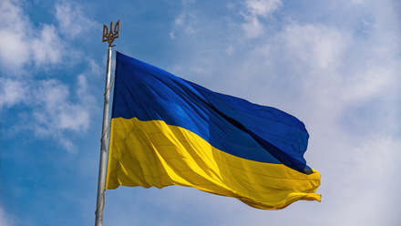 Ukraine flag flying in the wind in front of a blue sky with clouds. 