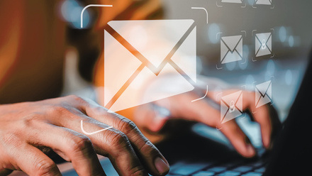 A pair of hands on a black laptop keyboard, hovering above are CGI envelope graphics in semi-opaque white.