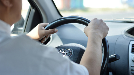 A driver wearing a white shirt and holding the steering wheel of a vehicle.