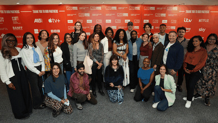 A diverse cohort of the TV Foundation's career programme participants standing in front of a red background.