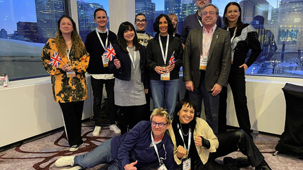 A group of 10 UK Indies delegates with Pact's Ross Lewis, posing for the camera with some mini-Union Jack flags in front of a large window.