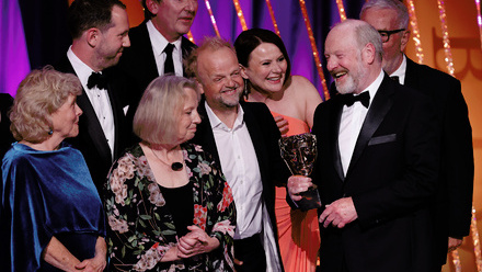 Photo of the Mr Bates vs The Post Office team on stage celebrating their win, with Sir Alan Bates holding the BAFTA trophy and smiling joyfully.